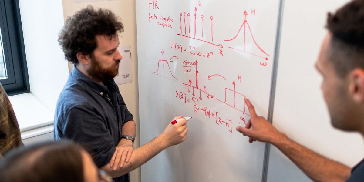 Team members actively discussing and solving a problem on a whiteboard, embodying shared challenge.